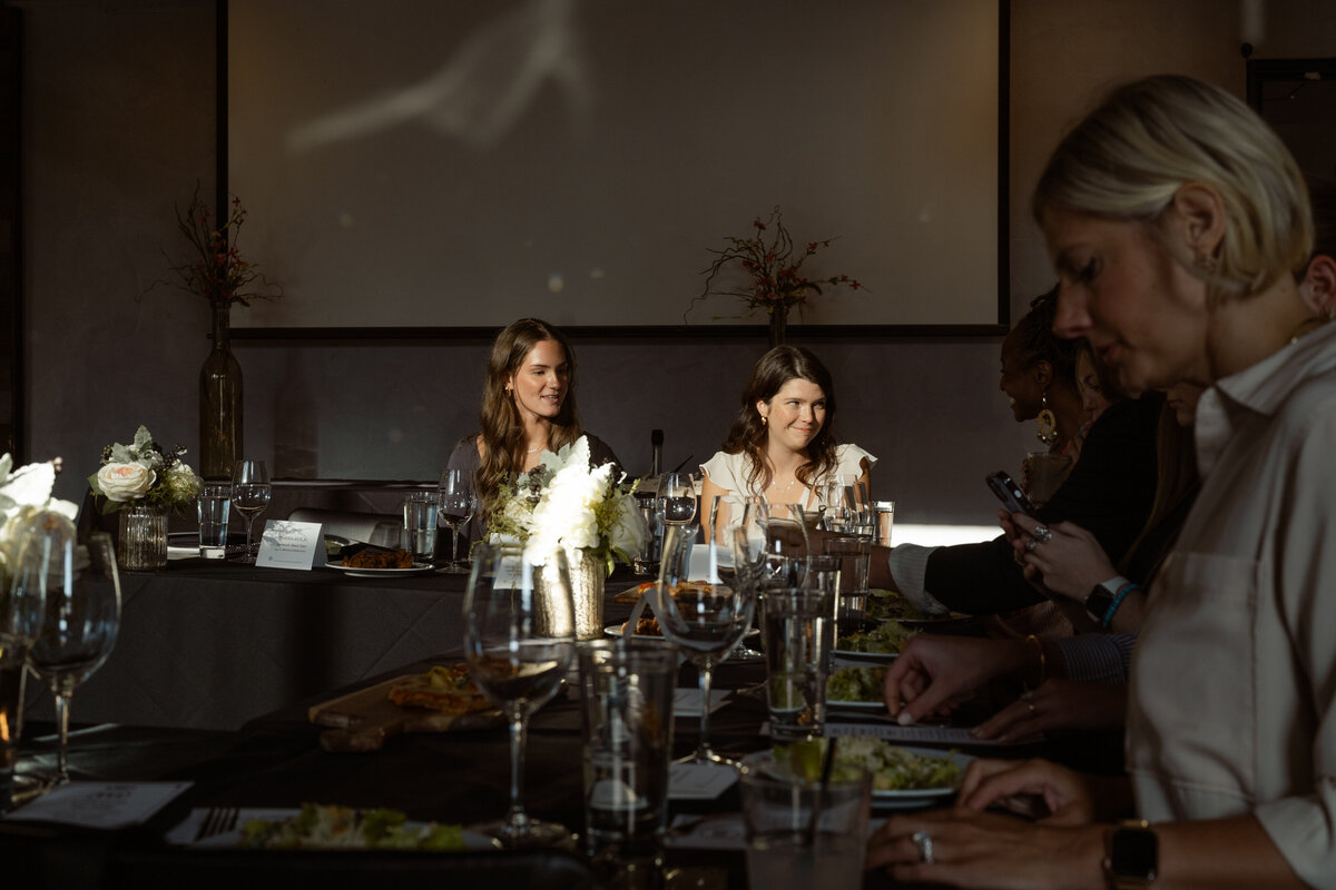 Bathed in golden hour light, an attendee smiles warmly at another guest during the networking dinner. The vibrant contrast of the sunlight highlights her expression and adds a glowing energy to the interior of STIRR Dallas.