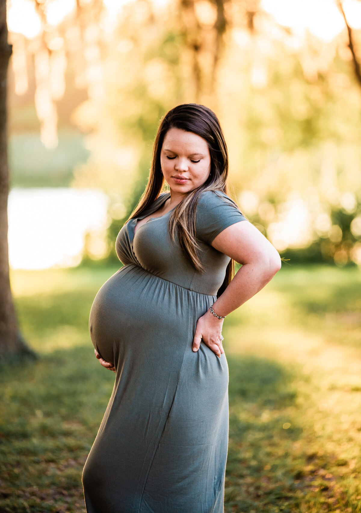 A mom wearing an olive green dress holds her baby bump at Bay Area Park.