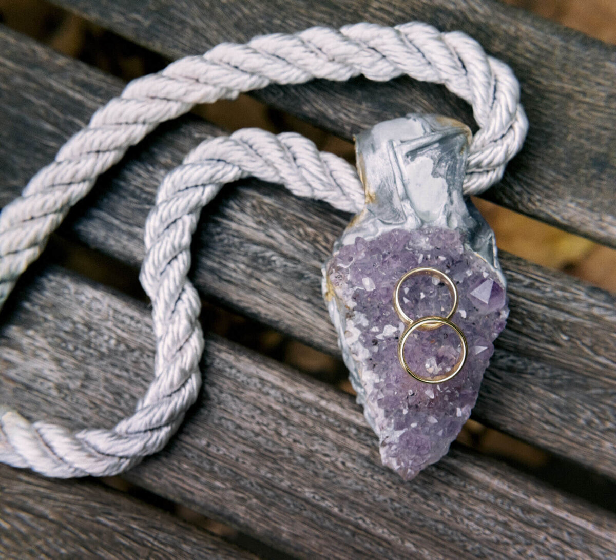 Two wedding rings are placed on top of a purple-colored stone necklace. NYC City Hall Elopement Image by Jenny Fu Studio