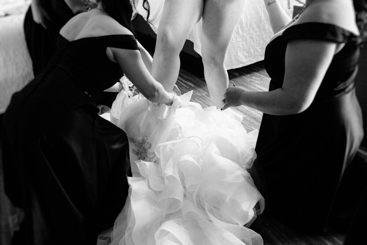 black-and-white-portrait-of-bridesmaids-helping-the-bride-getting-in-her-dress-1