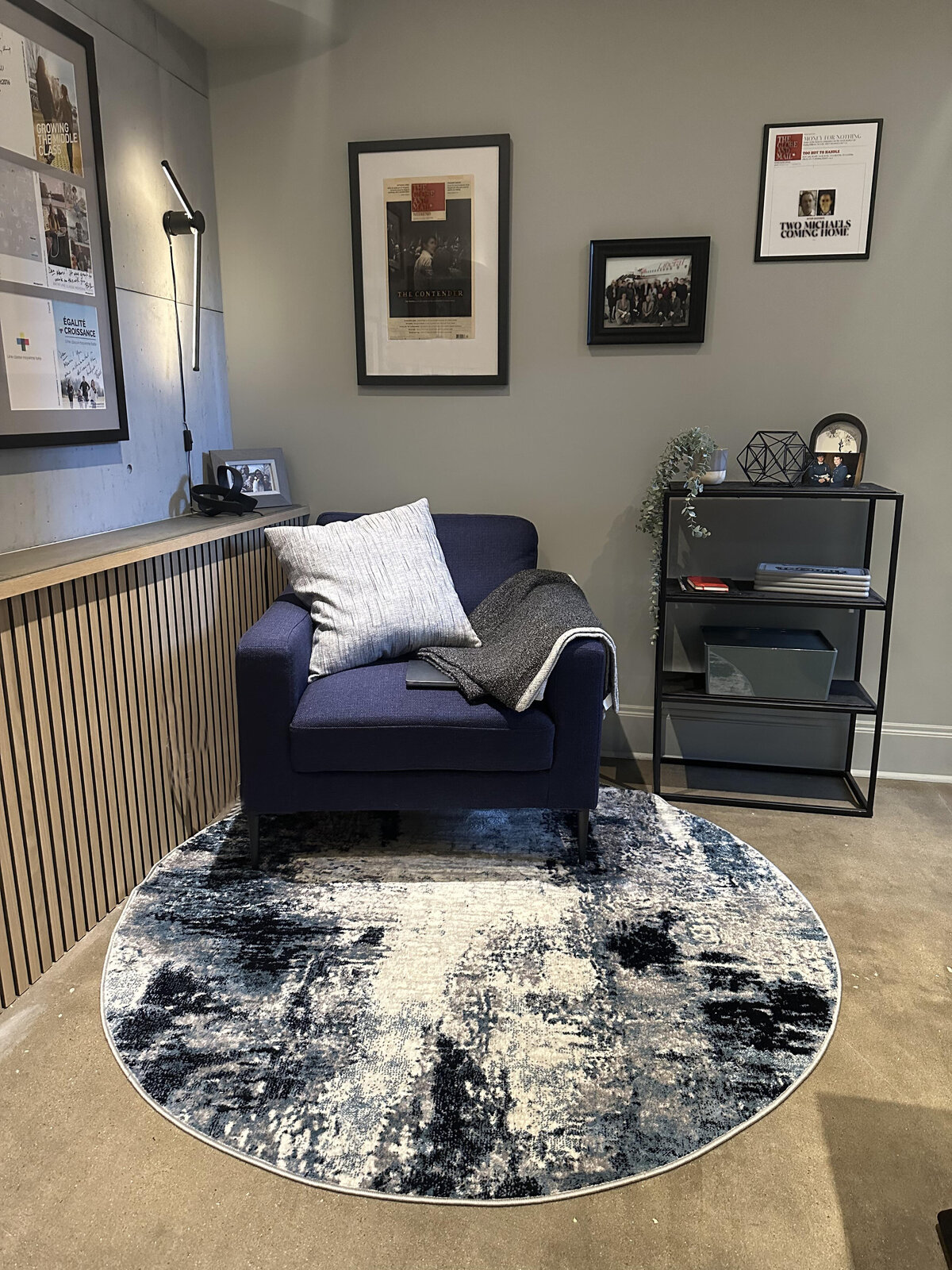 Cozy yet masculine home office seating area with blue armchair, distressed industrial abstract rug and black metal shelving designed and installed by Urbanomic Interiors, Westboro (Ottawa).