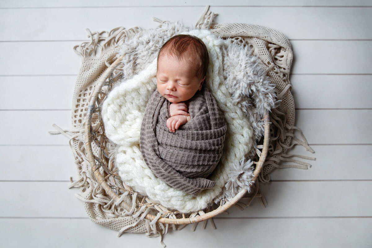 Portrait of a newborn baby  snuggled in a gray wrap and laying in a basket