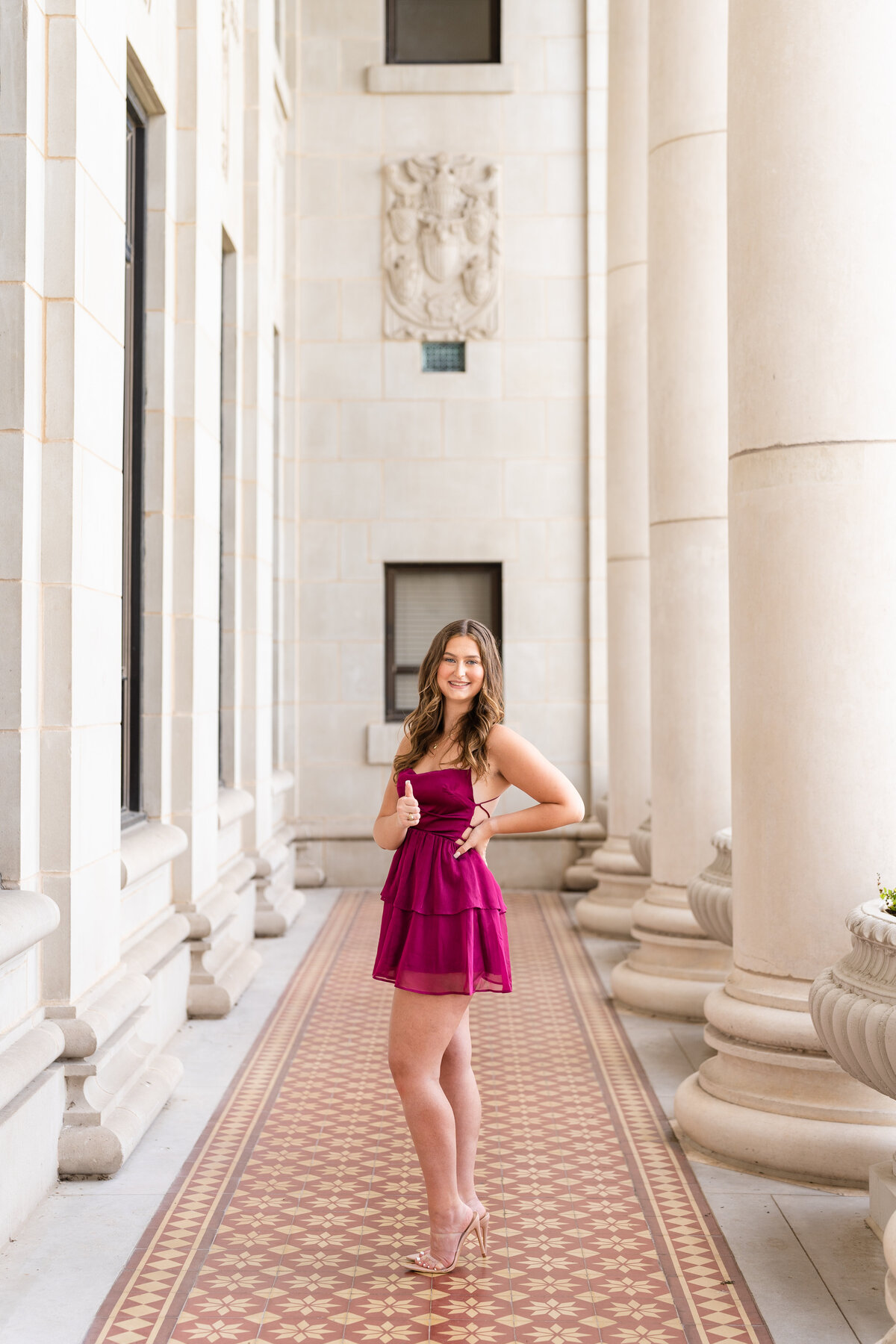Texas A&M senior girl with hand on hip and thumbs up in maroon dress in columns of Administration Building