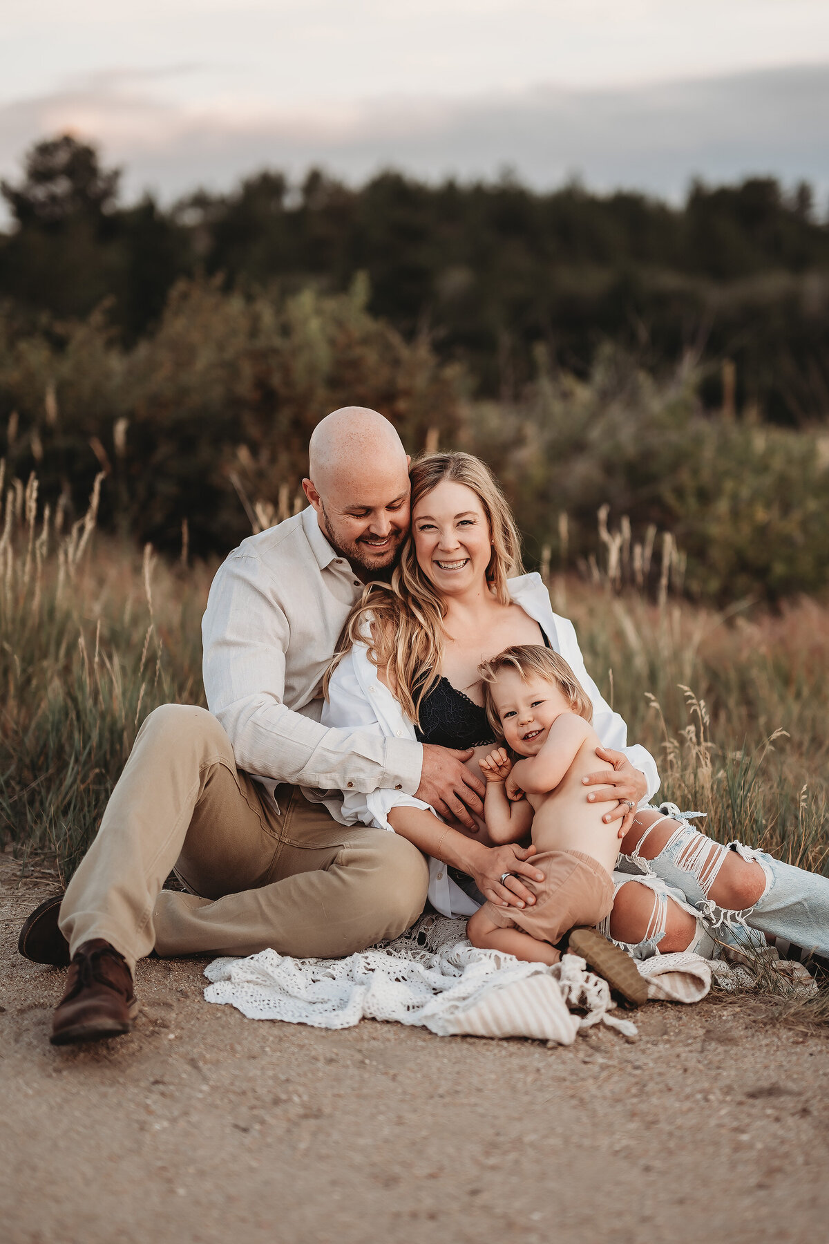 family sitting on the ground with boy snuggling mom's maternity belly