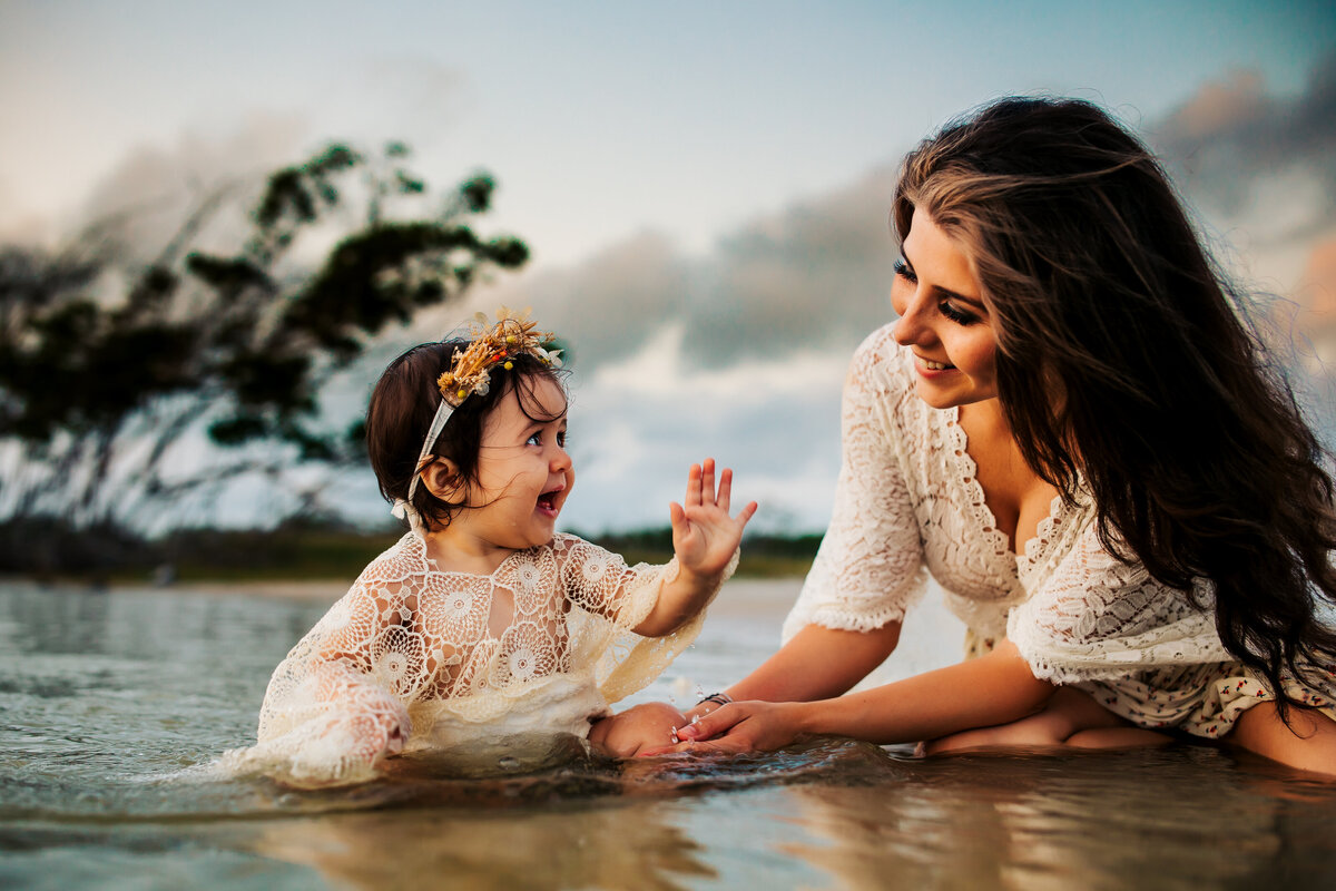 mother and daughter sitting in water splashing and laughing