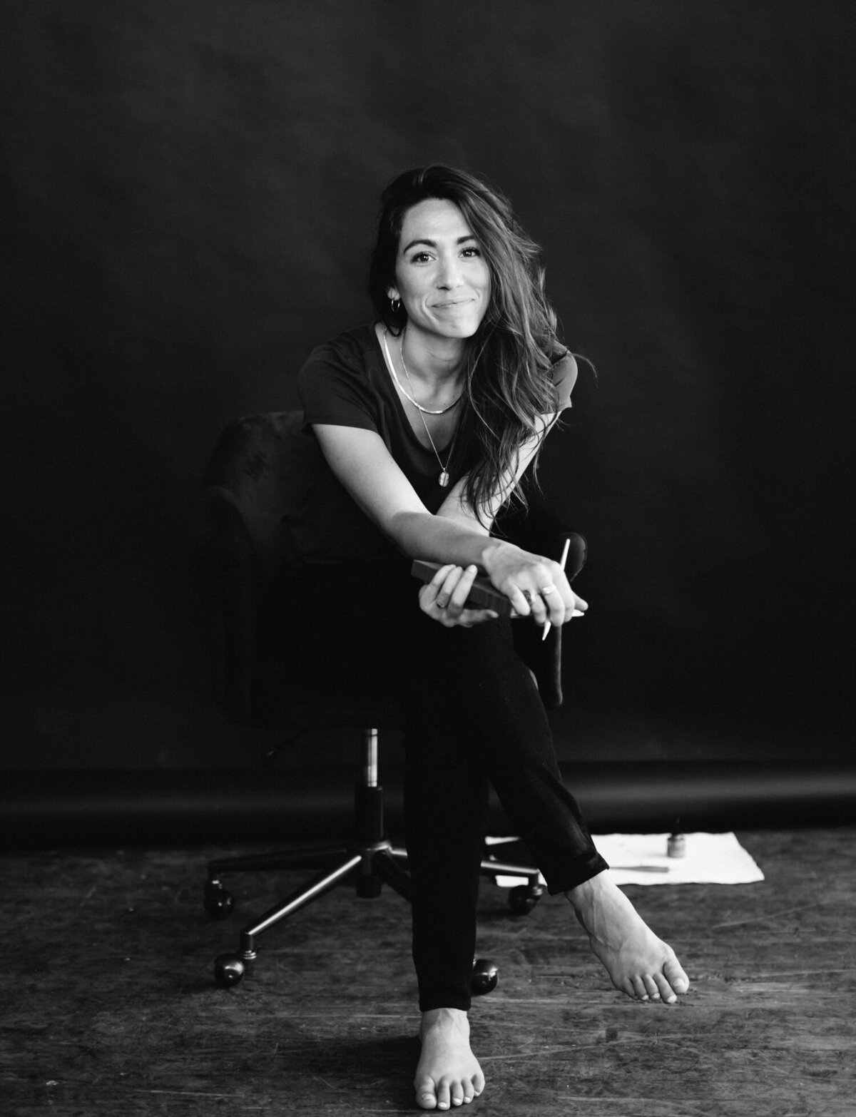 relaxed woman with long hair in chair, black studio backdrop, brand photography session