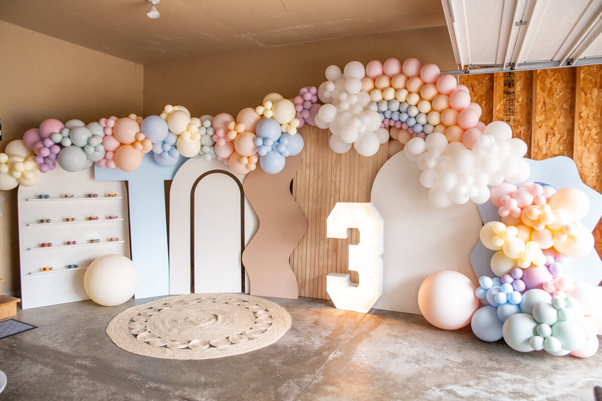 Pastel balloons set up on wooden backdrops and a giant 3 marquee number.
