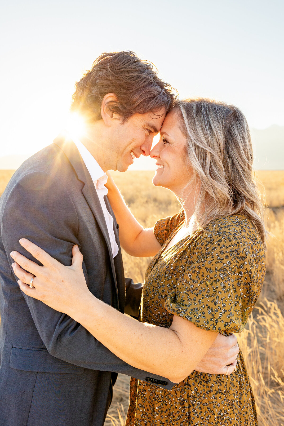 A husband and wife lean in forehead to forehead, bathed in the warm glow of the setting sun in a golden grass field.