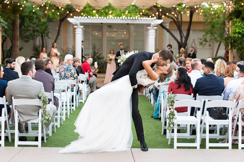 A groom dipping a bride and kissing her at the end of an aisle.