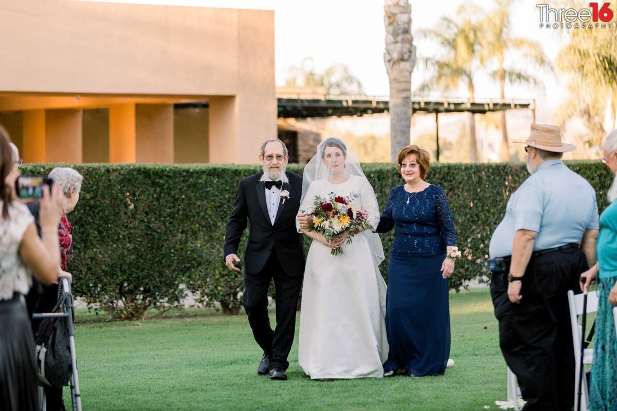 Bride being escorted by her parents down the aisle