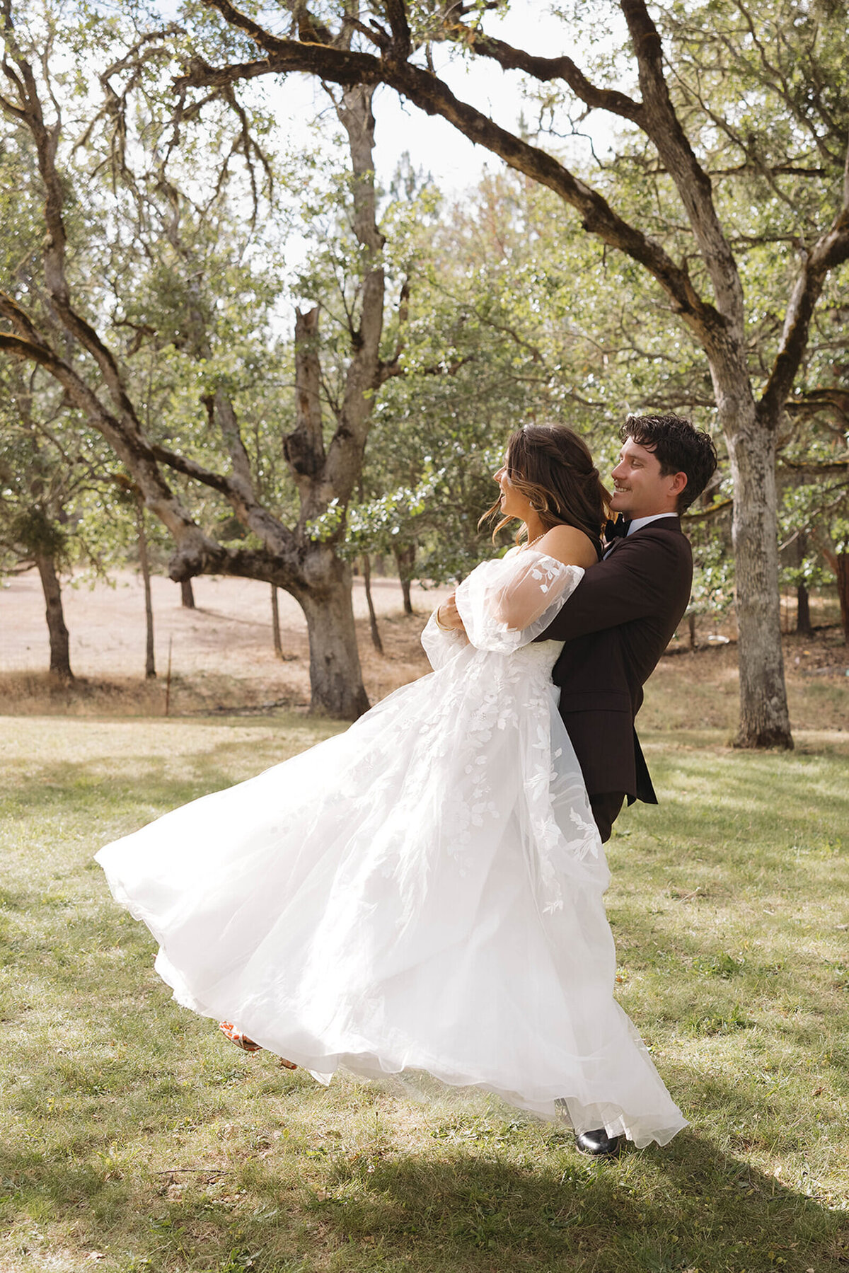Groom lifting and spinning his bride under the oak trees