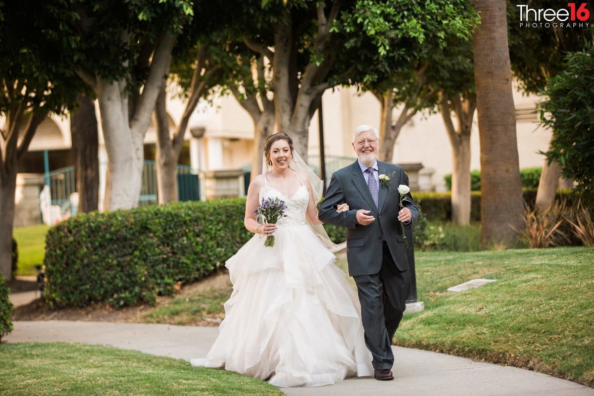 Bride and her father walk down the path heading towards the aisle