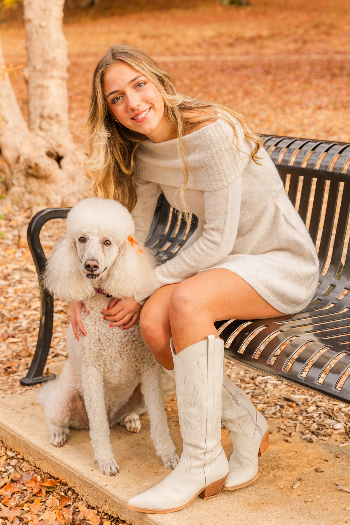 High school senior girl wearing a white dress and white boots sitting on a bench hugging her dog Atlanta park Laure Photography