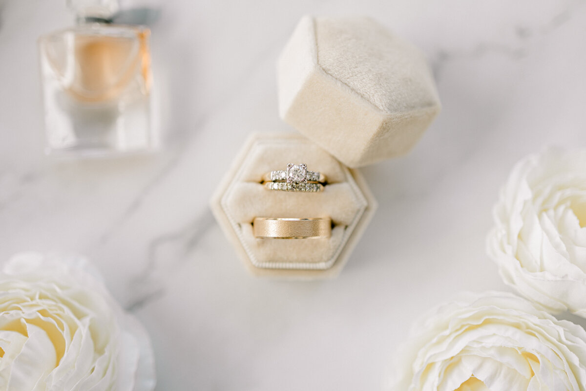 close up shot of wedding rings with perfume and flowers