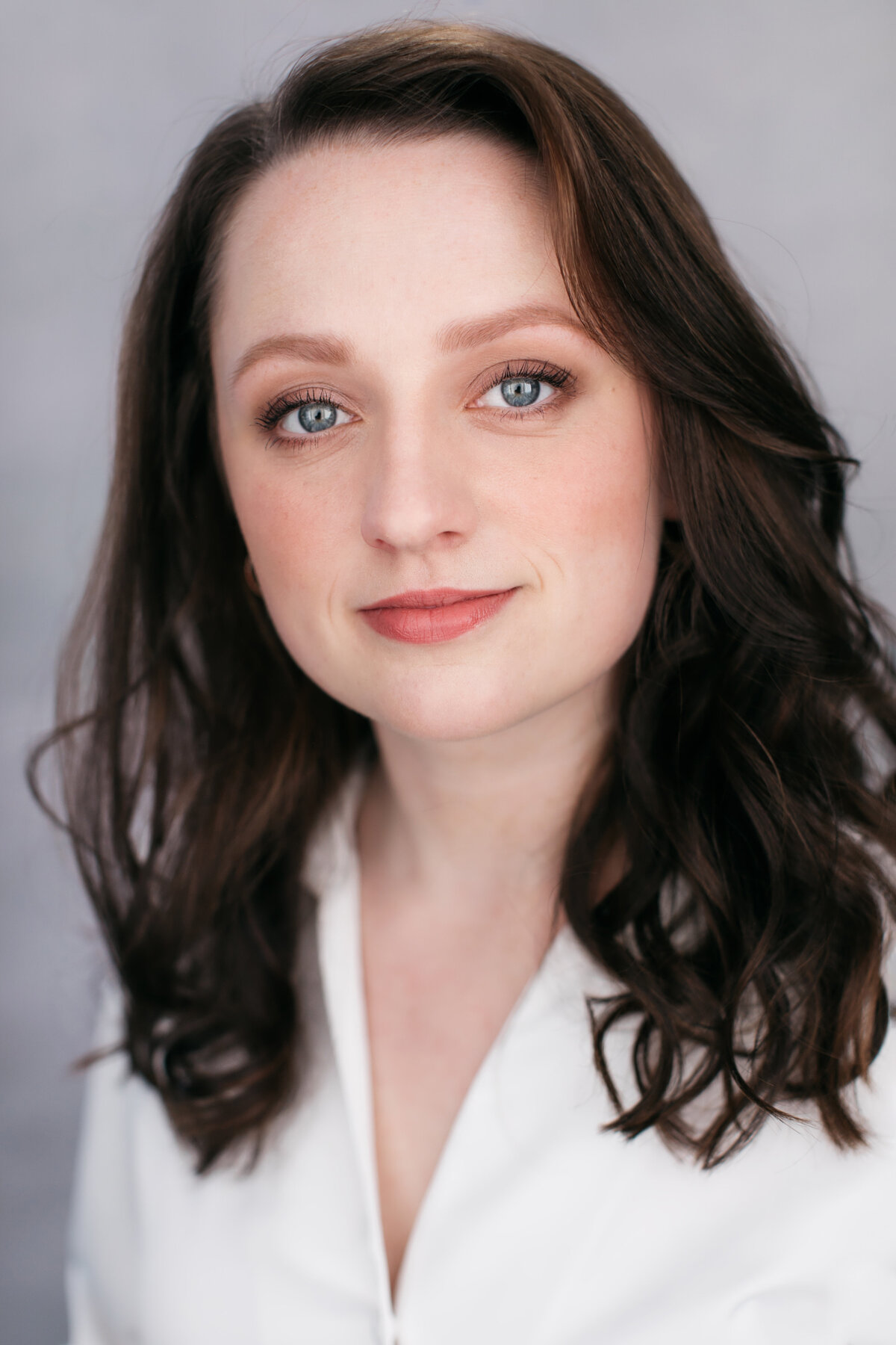 Castingfoto van Froukje Zuidema. Vrouw met donkerbruin haar en blauwe ogen voor lichtgrijze achtergrond.