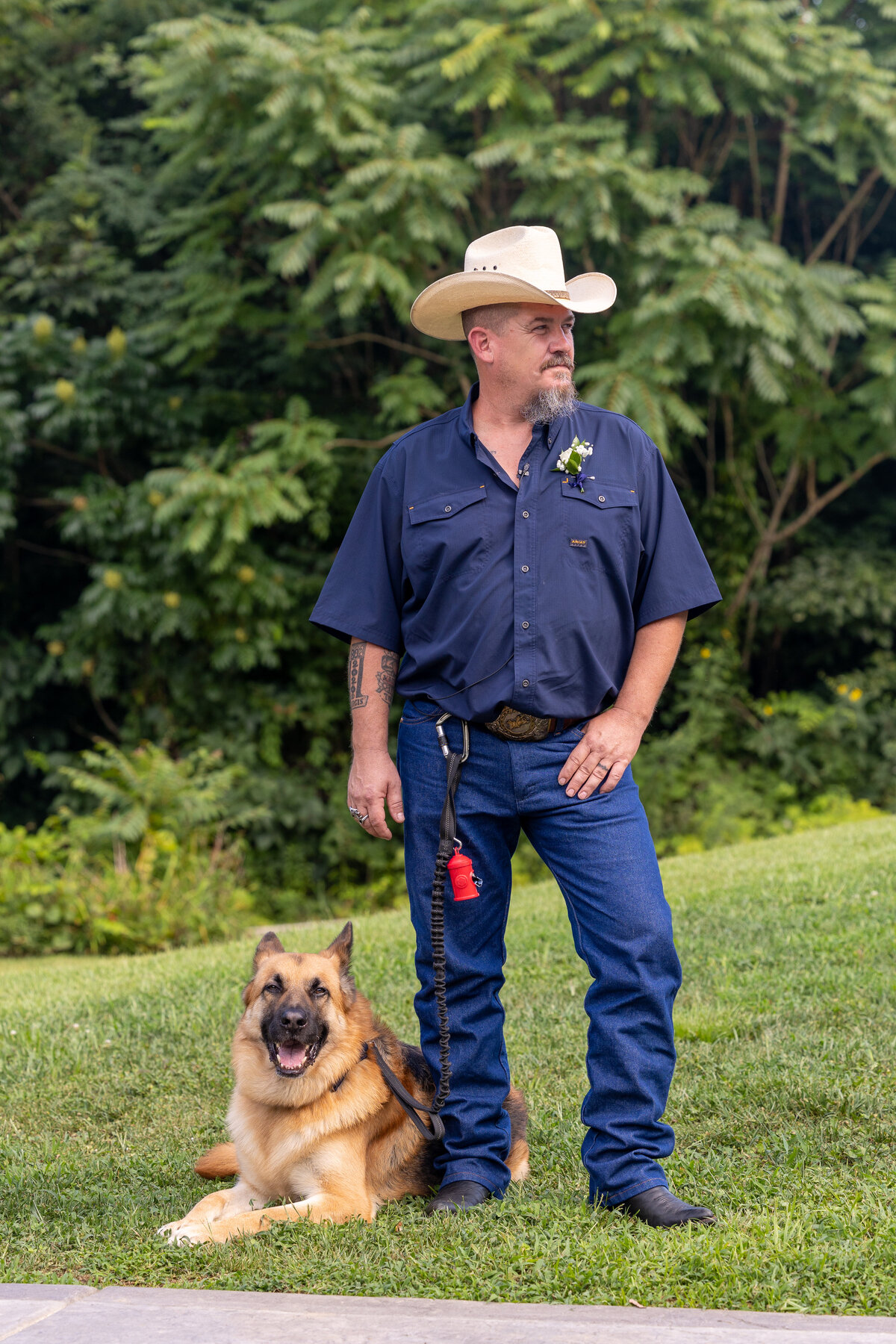 groom wearing blue jeans, blue button down shirt and white cowboy hat with his german shephard service dog sitting next to him in Columbus Georgia