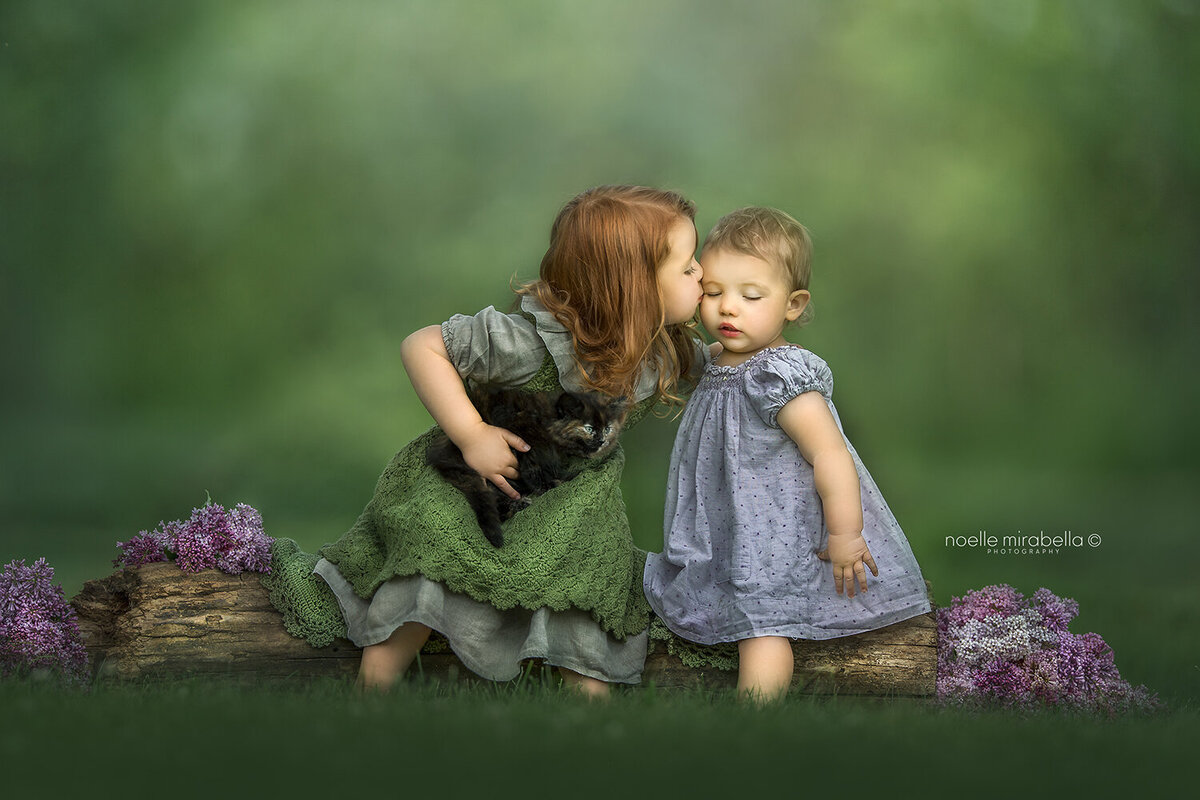 Girl kissing her baby sister on the cheek sitting outside in nature.