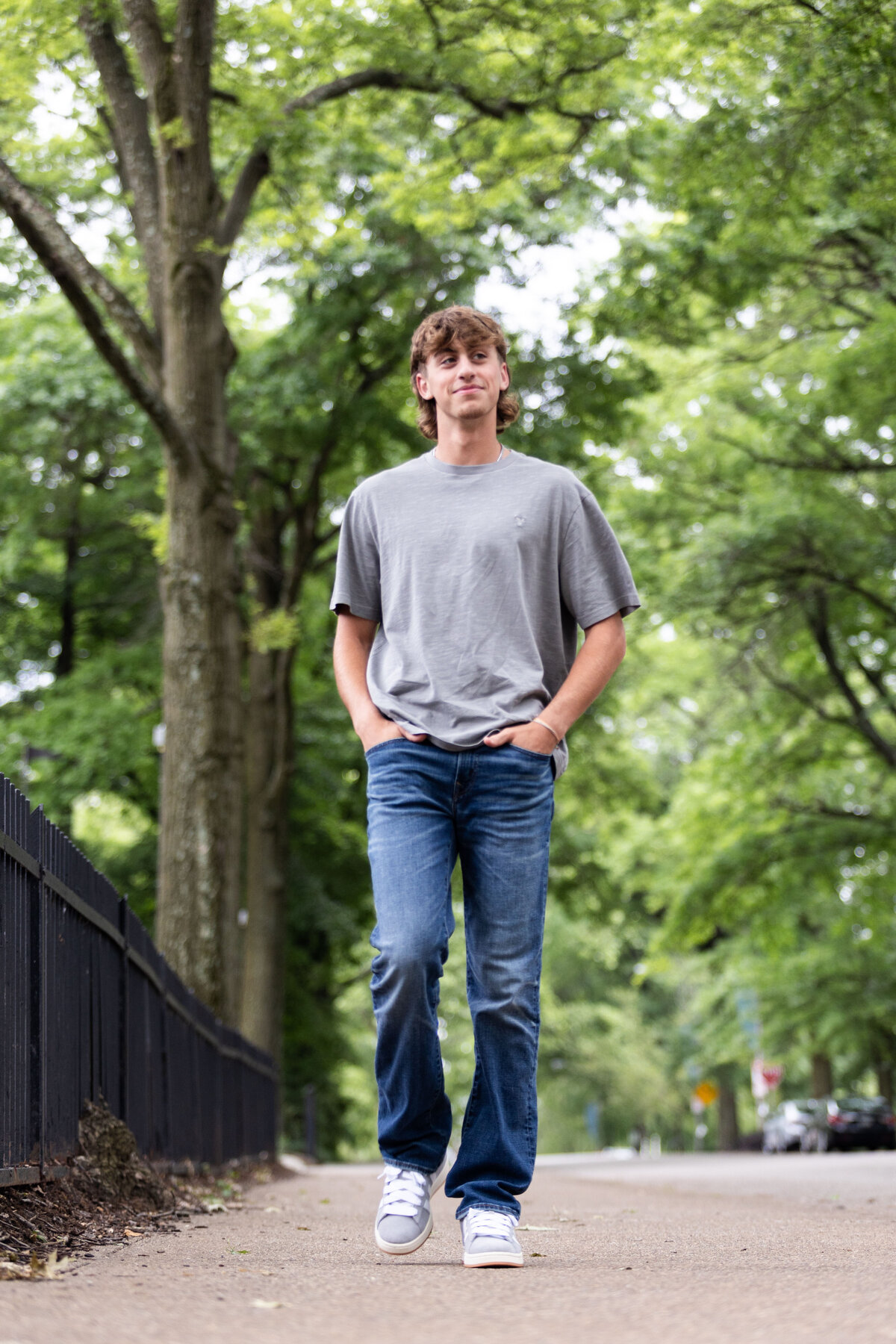 High school senior walks on side street with hands in pocket for his senior session with Melissa Helman Photography
