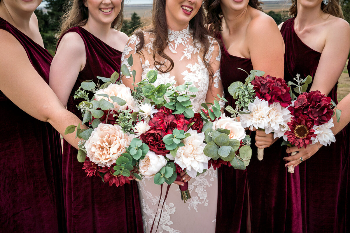 The bride and her bridesmaids gather their vibrant bouquets together, creating a stunning display of floral beauty at the North Coast Hitching Post in Loleta. This intimate wedding moment highlights the bond between the bride and her closest friends, set against the venue's rustic charm. Perfect for capturing timeless wedding memories in Humboldt County.