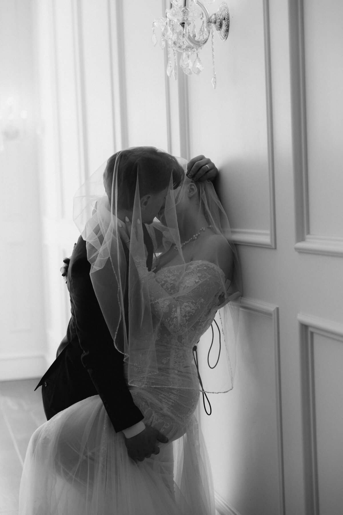 Veil kiss against wall under chandelier