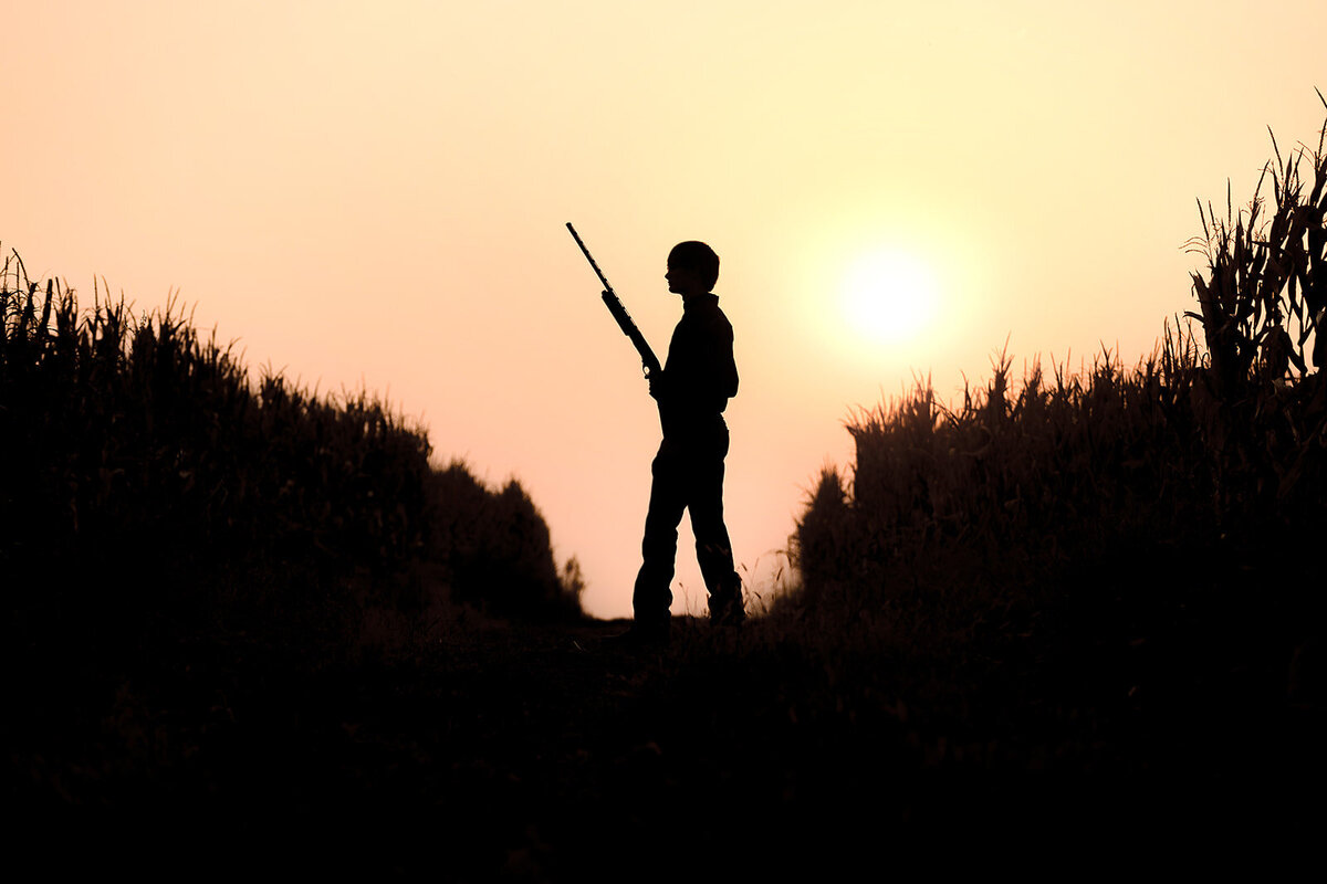 Silhouette senior male with gun in field