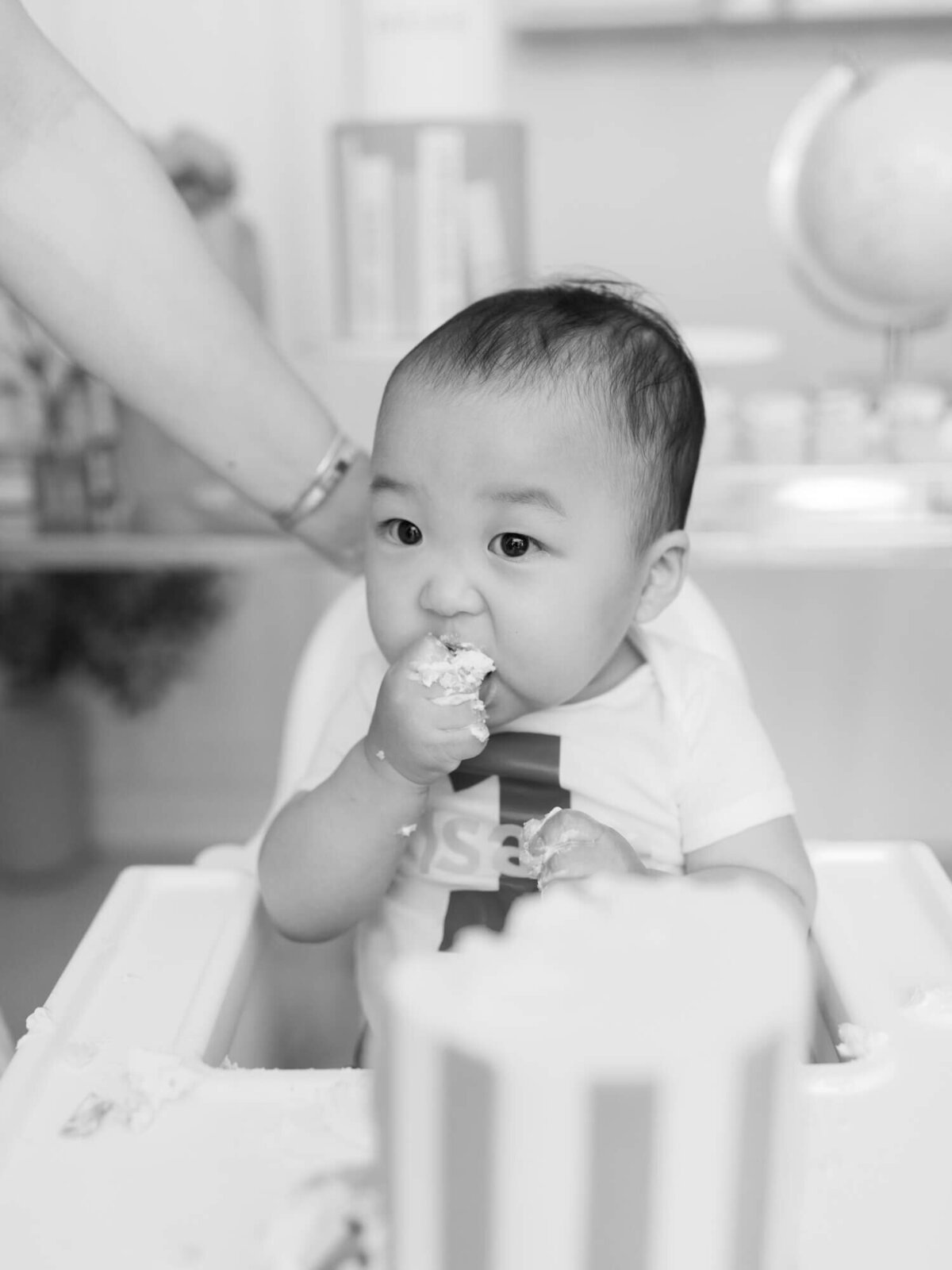 black and white photo of baby eating first birthday smash cake