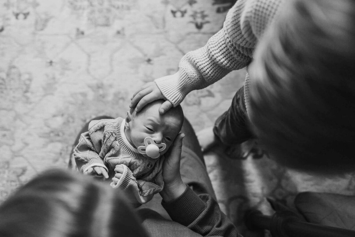 Older sibling gently touch their newborn brother's head during a tender lifestyle photography session.