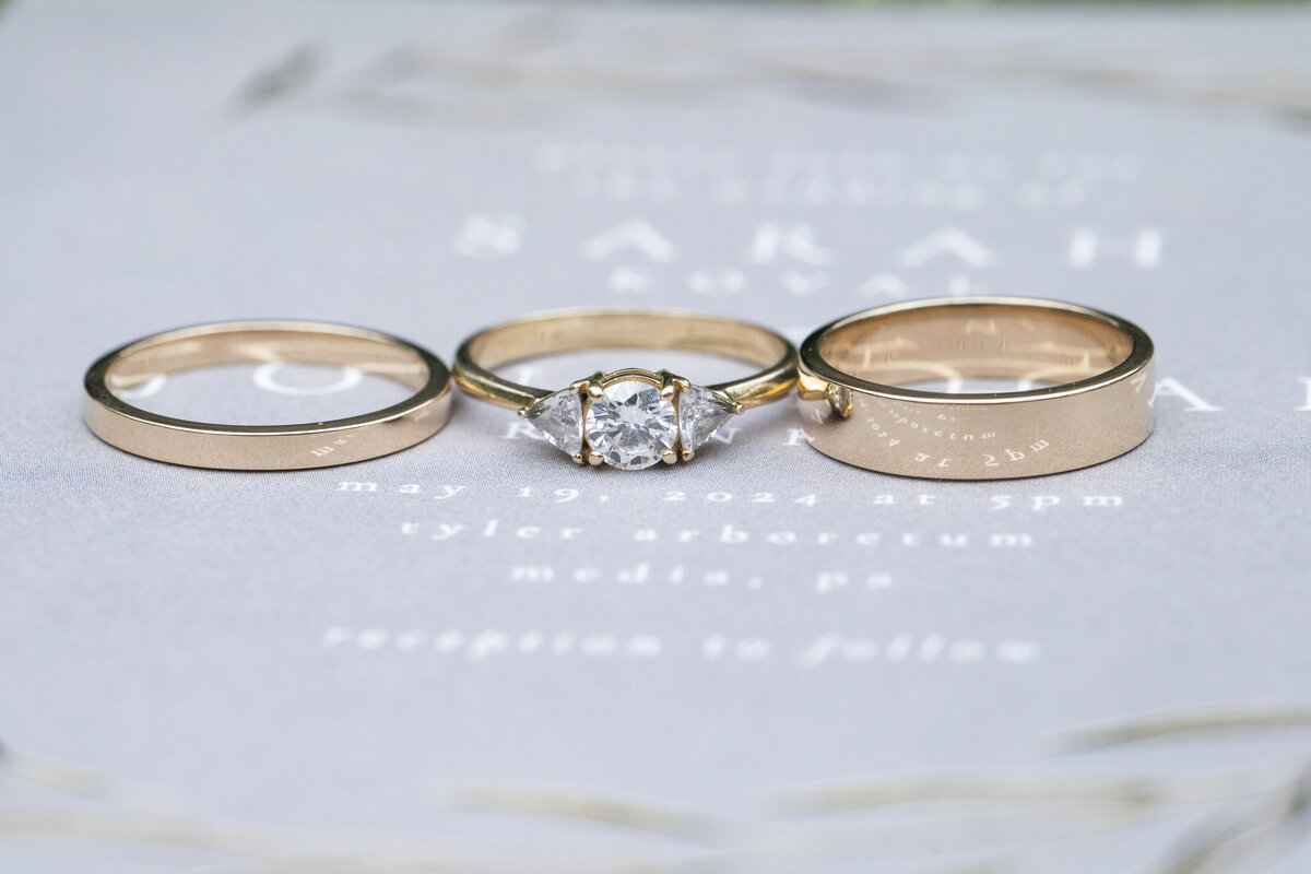 close up shot of wedding rings laid on the wedding invitation. Tyler Arboretum in Pennsylvania