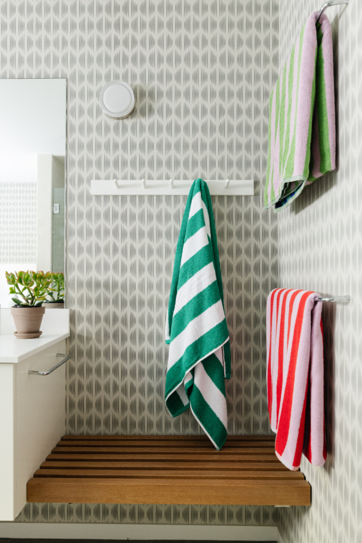 The kids' bath in this Main Street Hingham home features a floating teak bench, Schumacher wallpaper, simple light fixtures, and bold striped towels. As seen in Boston Globe magazine.