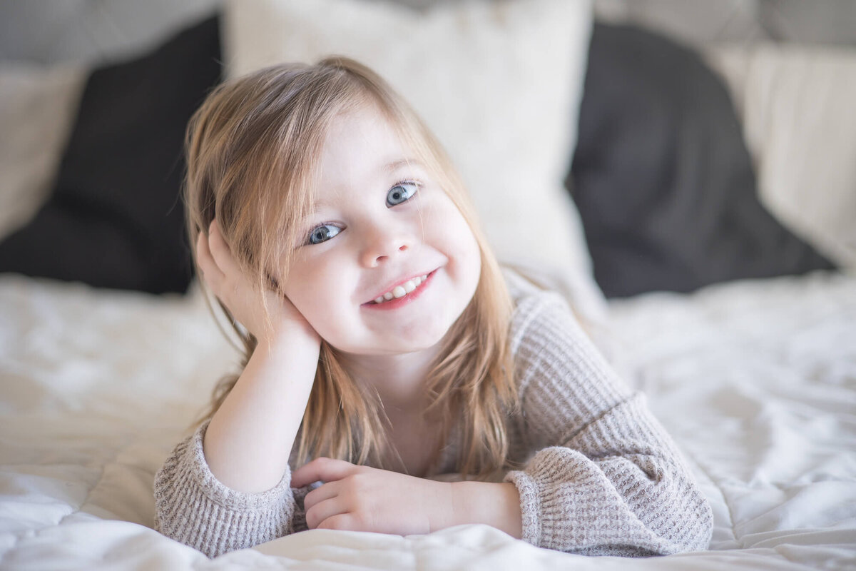 adorable toddler girl happily smiling on a bed with her hand holding her head up