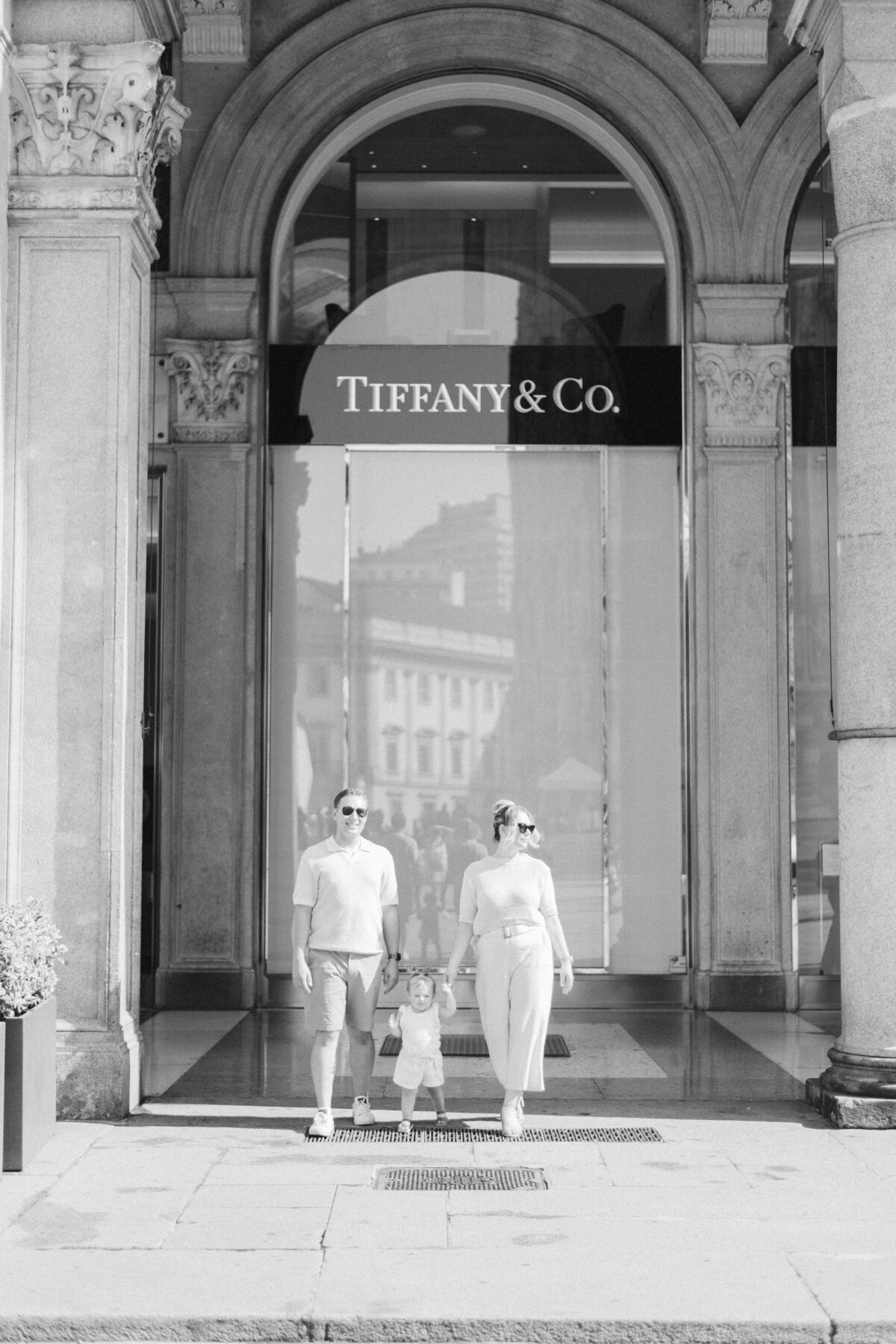 Stylish family of three holding hands in front of Tiffany & Co. in Milan italy during a sunlit morning