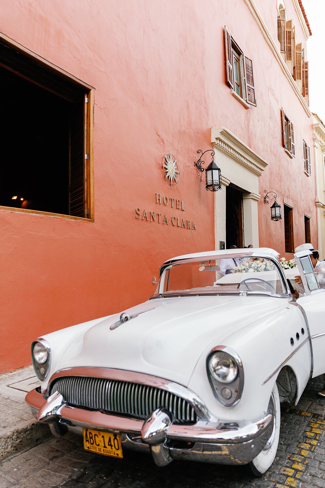 A classic white vintage car parked outside Hotel Santa Clara, a romantic setting for Victoria and Daniel’s Cartagena destination wedding.