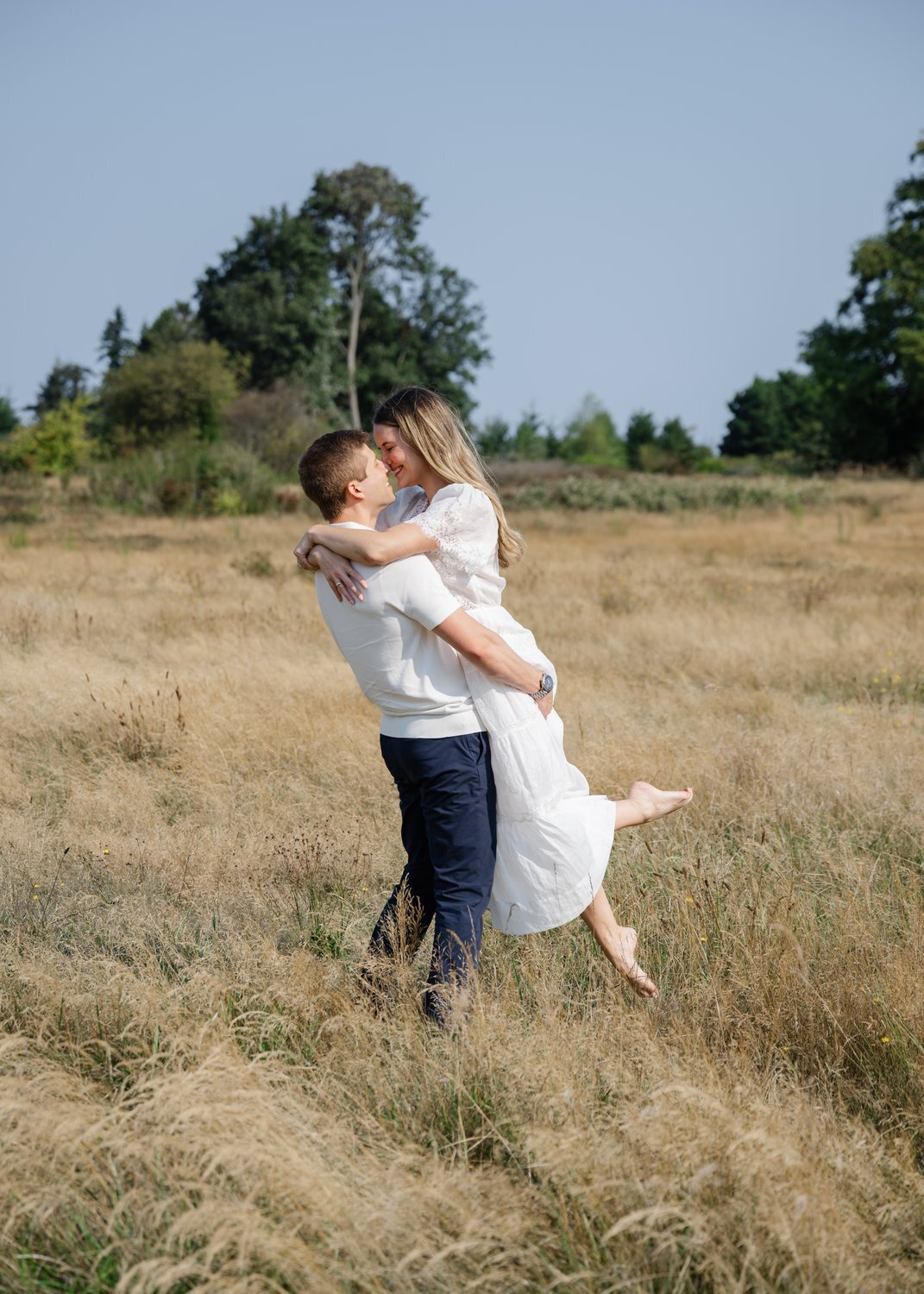 groom twirls bride with white dress in open field in seattle