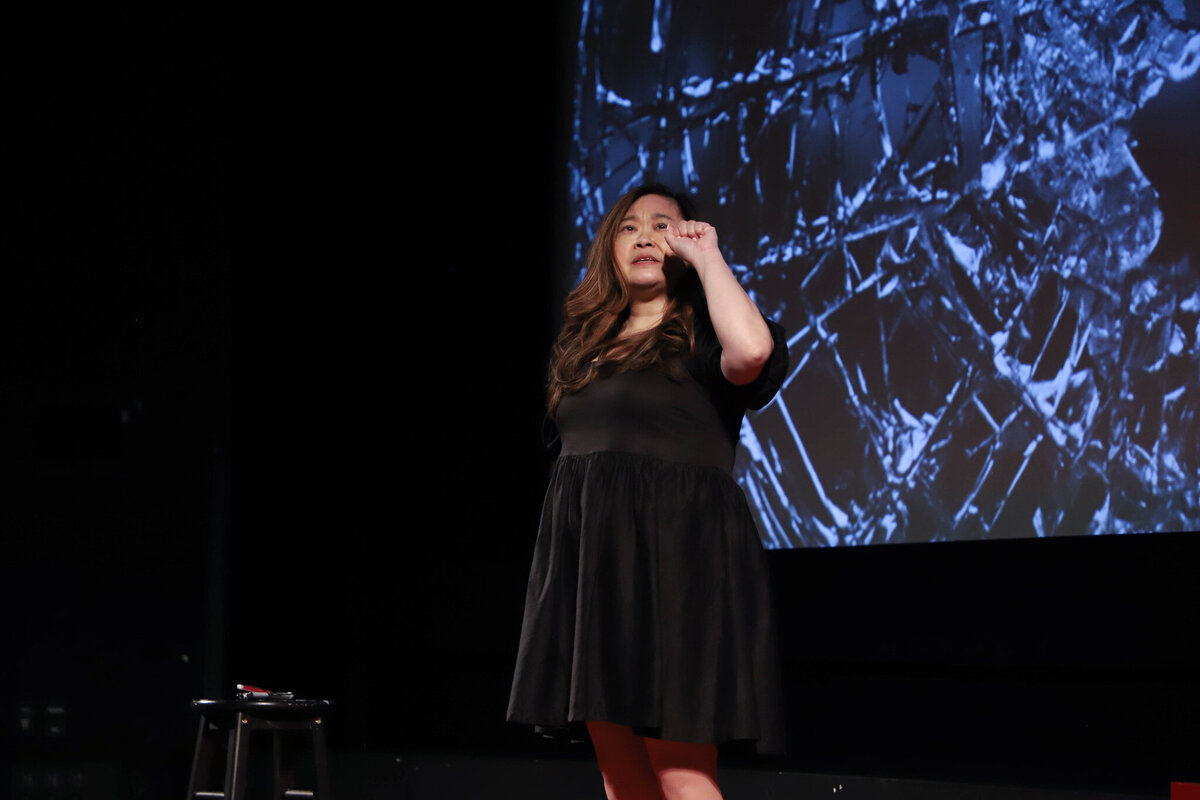 Anne looking out with her hands held in a fist motion while an image of shattered glass is behind her