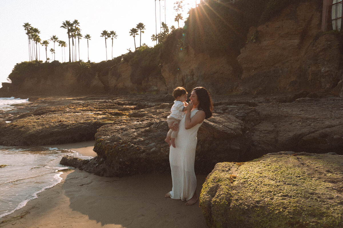 Mom standing on the rocks at Shaw’s Cove holding her baby during a Laguna Beach family session.