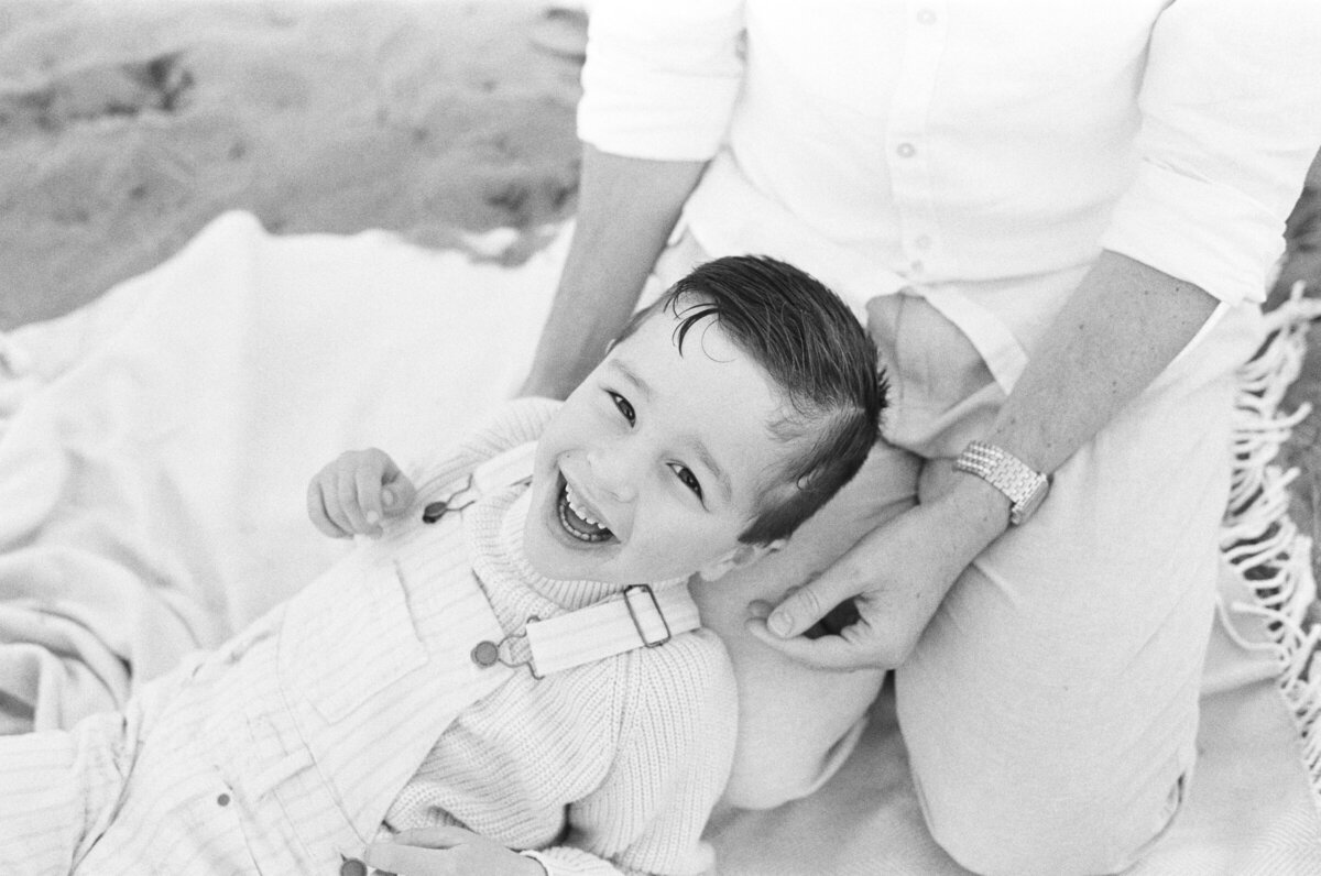candid smiling photo of toddler boy in dads lap on black and white film for these family photos in seattle 