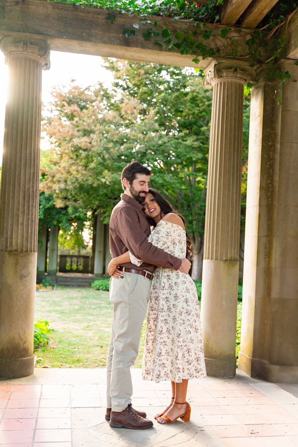 A white man and medium-skinned woman hug each other close underneath a stone structure in Harkness Memorial State Park