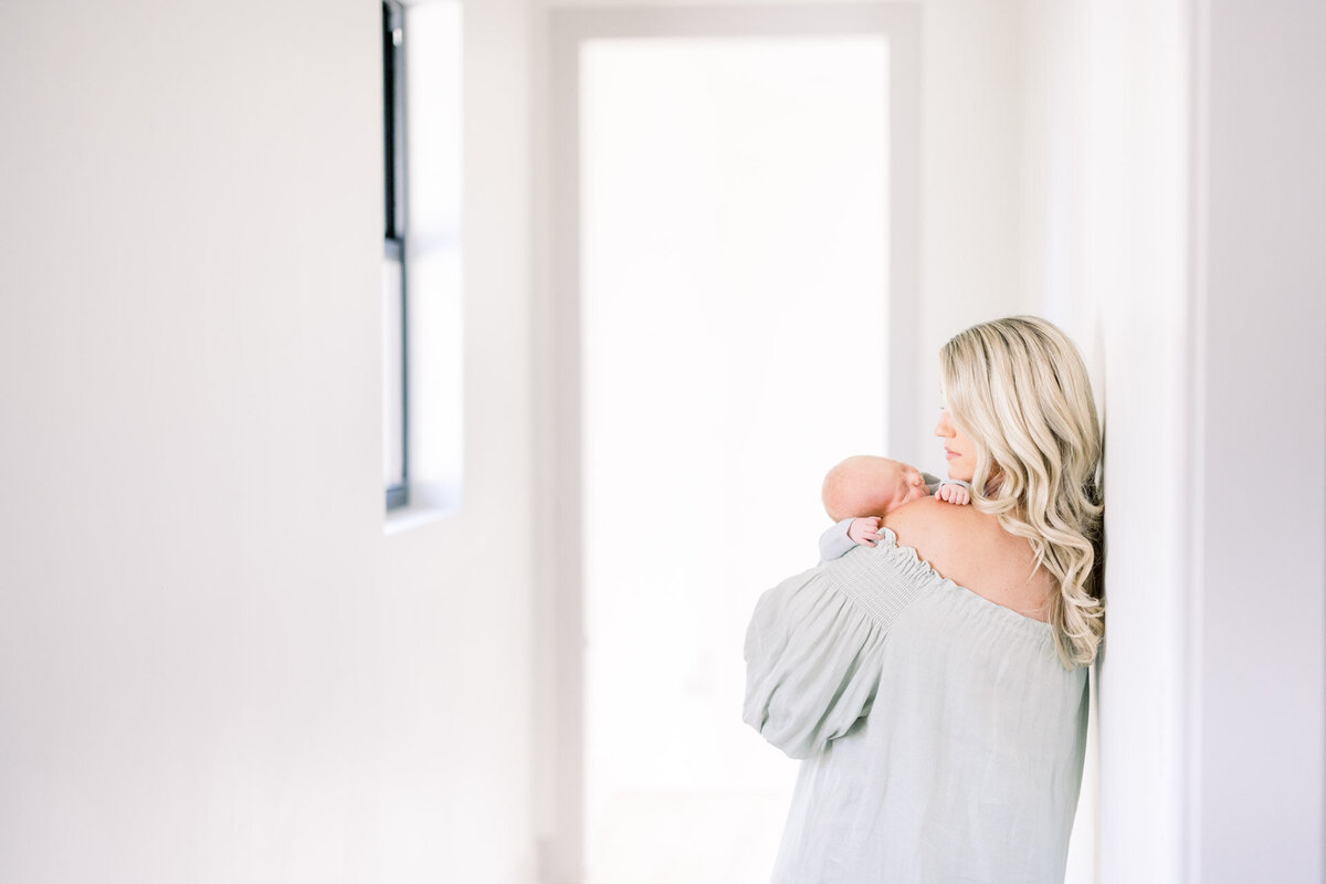 mom looking at baby on her shoulder in a hallway for Tampa newborn photographer Tina Marie Studio.