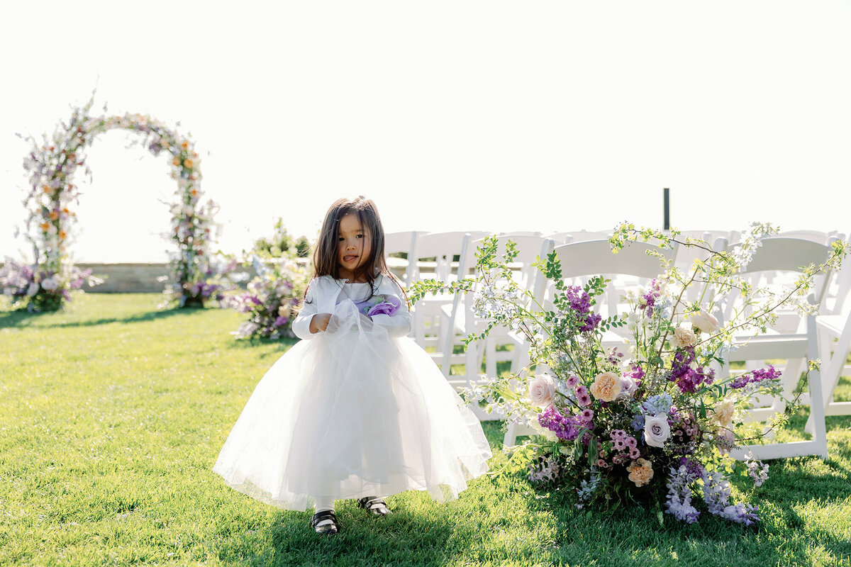 floral ceremony arch and flower girl next to aisle markers in shades of lavender and purple