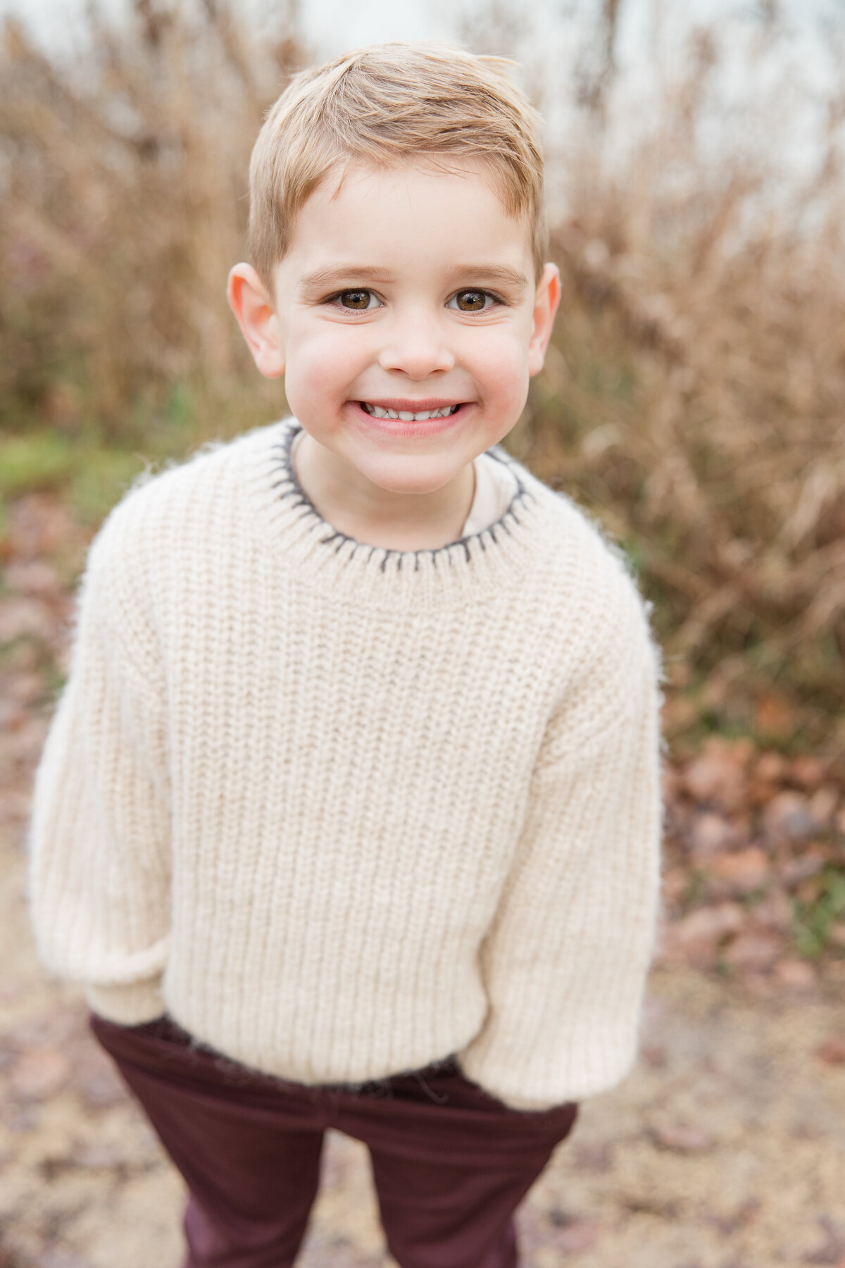 A little boy standing with his hands in his pockets and smiling