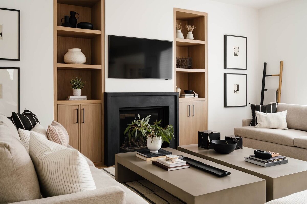 Modern living space with white oak built-in cabinetry and striking black concrete fireplace, complemented by high-contrast white and black furnishings and artwork.