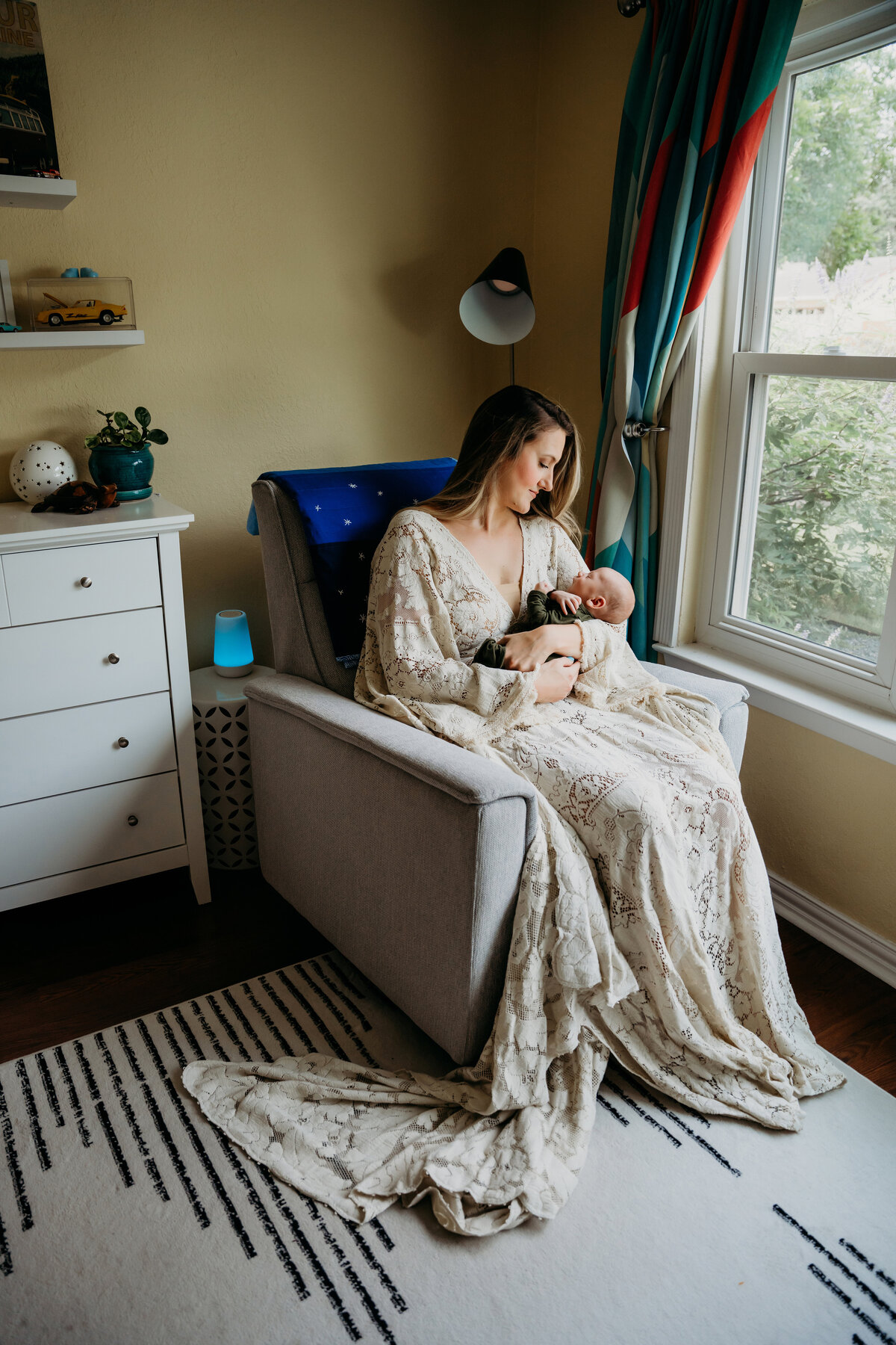 Newborn Photographer, a mother sits in a corner of the room with baby, admiring him