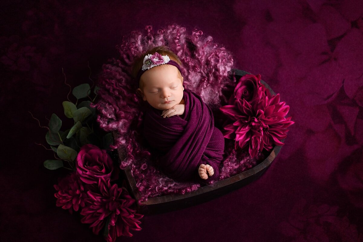 Baby girl in raspberry pink wrapped with toes peeking out in heart bowl.