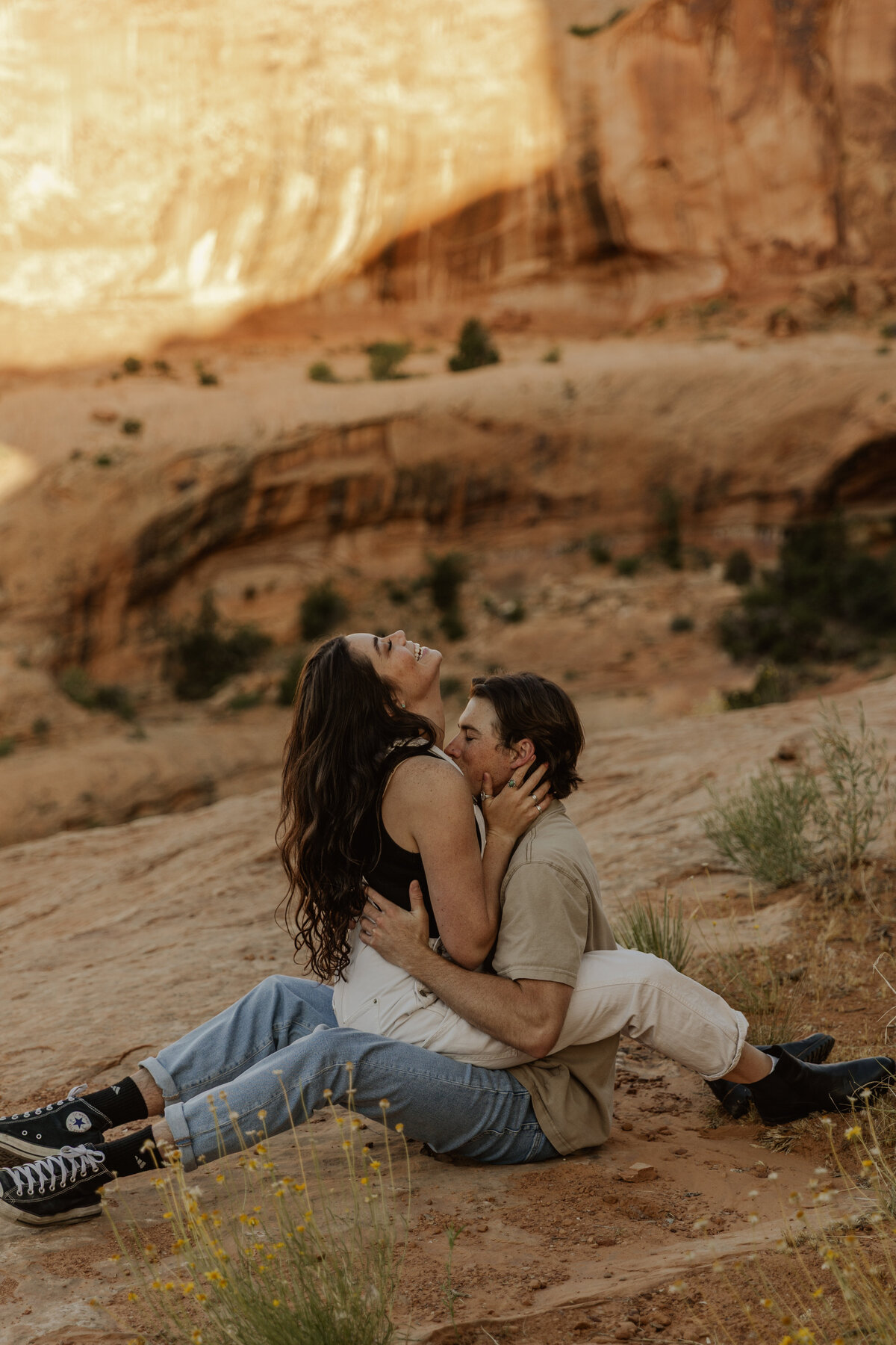 Couple Sitting in the Utah Desert Kissing and Laughing in the Red Rocks 