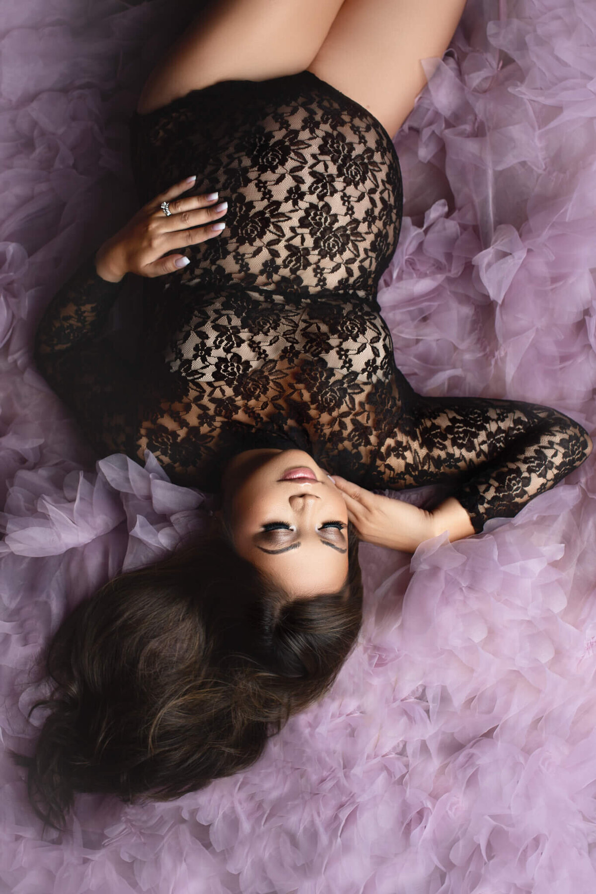 pregnant mother in black lace bodysuit laying on her back, surrounded by purple tulle at hamilton, ON maternity studio