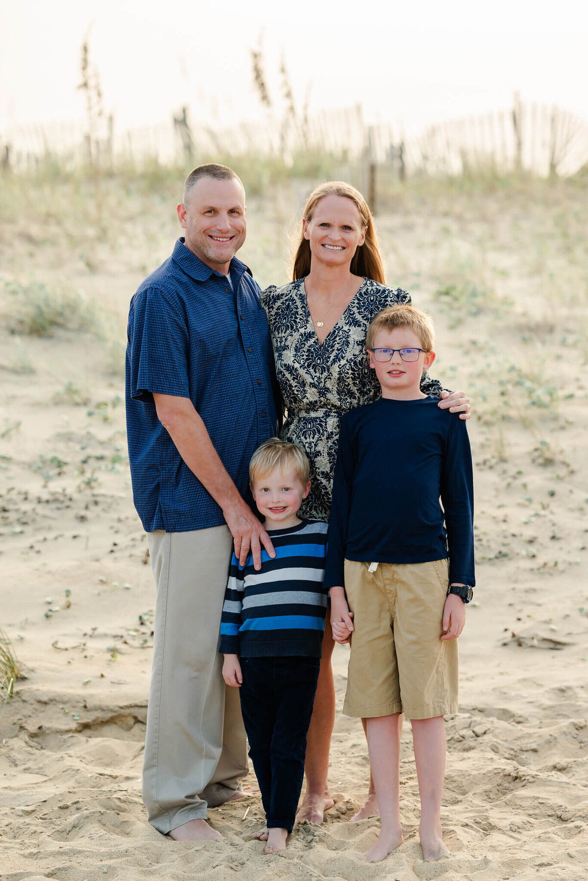 Two brothers put their arms around each other while their parents do the same behind them at an Outer Banks family session on the beach.