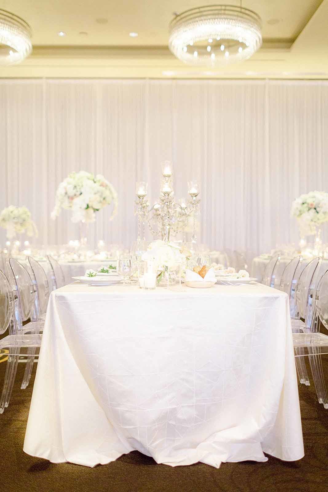 wedding reception table with white linen, clear ghost chairs, crystal candelabra, large orchid centerpiece, white wall draping at Four Seasons Hotel