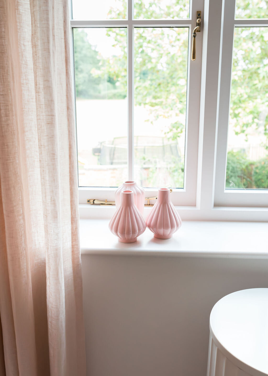 Decorative pink vases sit on a white windowsill adorned with soft pink drapes.