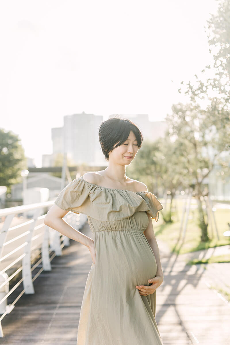 Woman placing one hand on her belly and the other on her waist and posing for her light and airy, beautiful maternity photograph