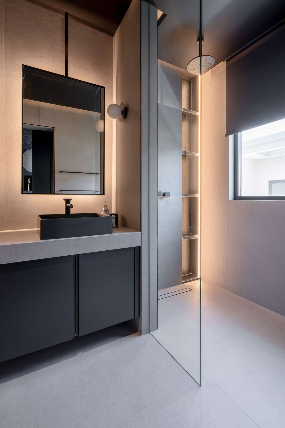 Modern grey bathroom with dark cabinets, grey counters, and a chic black sink. To the right is a glass partition and a spacious walk-in shower.